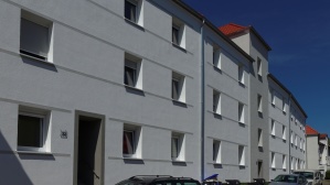 Sanierte Wohnhäuser mit drei Etagen an einer Straße, helle Fassade.