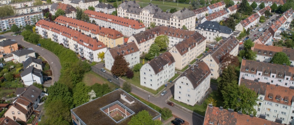 Unterschiedliche Gebäudetypen (Flachdach, Altbauten, Kasernenbauten, Einfamilienhäuser). Umliegend Wälder.