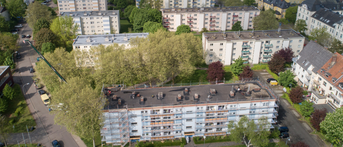 Mehrere Flachdachgebäude mit drei Etagen, dazwischen viele Grünflächen und Bäume.