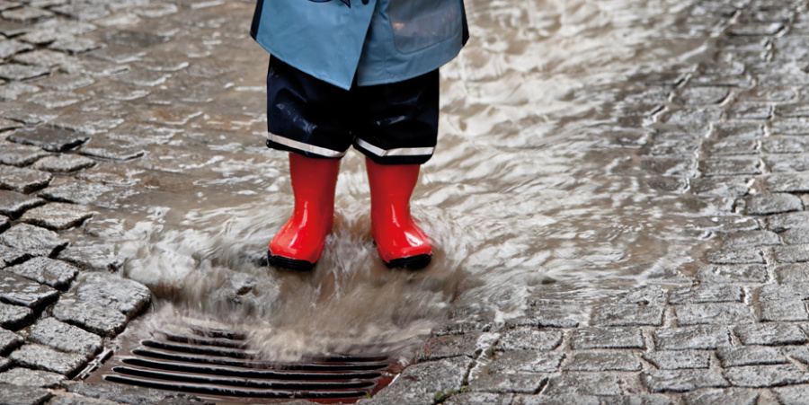 Kind in Regenstiefeln steht vor einem Gully. Foto: G.Sanders, Fotolia