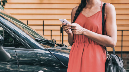 Dame in rotem Kleid mit Smarthone vor einem Auto