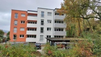 viergeschossiges Wohnhaus mit Flachdach, Balkonseite, während Umbau. Fassade braun und weiß.