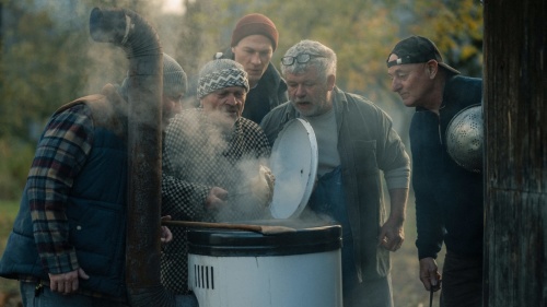 Fünf Männer stehen draußen vor einem Ofen. Der eine hält in der einen Hand den Deckel und in der anderen ein großes Stück Fleisch am Spieß, auf das alle schauen. Fünf Männer stehen draußen vor einem Ofen. Der eine hält in der einen Hand den Deckel und in der anderen ein großes Stück Fleisch am Spieß, auf das alle schauen.