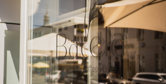 Außenansicht des Cafés Batela. Auf dem Fenster steht Batela und die Straße spiegelt sich. Außenansicht des Cafés Batela. Auf dem Fenster steht Batela und die Straße spiegelt sich.