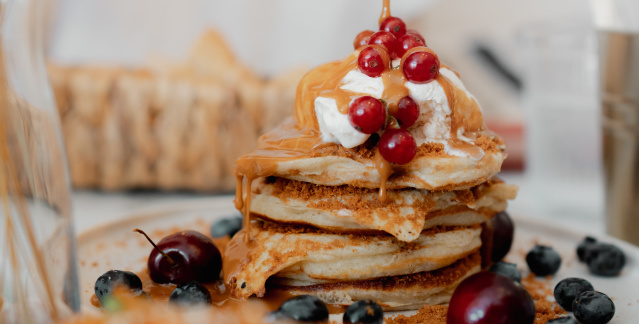 Eine Hand schüttet Sirup aus einem Gläschen auf Pancakes. Eine Hand schüttet Sirup aus einem Gläschen auf Pancakes.