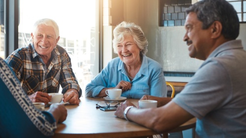 Senioren im Gespräch Vier Senioren sitzen an einem Tisch, unterhalten sich und lächeln