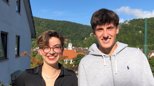 Tandem 2025/2026: Juliette Beaudou und Yann Ristic Eine junge Frau mit Brille und kurzen Haaren sowie ein junger Mann lächeln in die Kamera