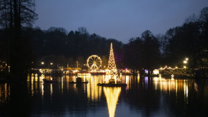 Impressionen vom Weihnachtsgarten 2025: Freitag Blick über den See auf den schwimmenden Weihnachtsbaum, Marktlichter und das Riesenrad bei einbrechender Dunkelheit.