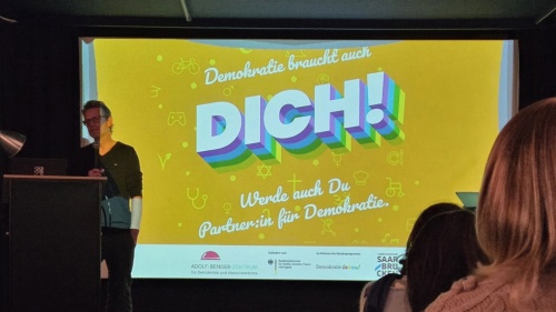 Mann vor einer Leinwand mit der Aufschrift Demokratie braucht dich