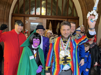 Mehrere kostümierte Personen mit einem Mann im bunten Kostüm und einem großen Schlüssel. 