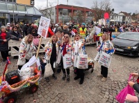 Zwei kostümierte Männer machen ein Selfie, während Konfetti durch die Luft fliegt und Menschen im Hintergrund feiern.