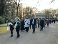 Prozession von der Gedenkfeier in der Neuen Halle auf dem Saarbrücker Hauptfriedhof zur Kranzniederlegung. Im Vordergrund sieht man zwei Personen, die Kränze tragen und weitere Personen, unter ihnen Saarbrückens Oberbrürgermeister Uwe Conradt, die ihnen f