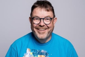 Ein Mann mit einem blauen Shirt und einer Brille grinst breit in die Kamera. Ein Mann mit einem blauen Shirt und einer Brille grinst breit in die Kamera.