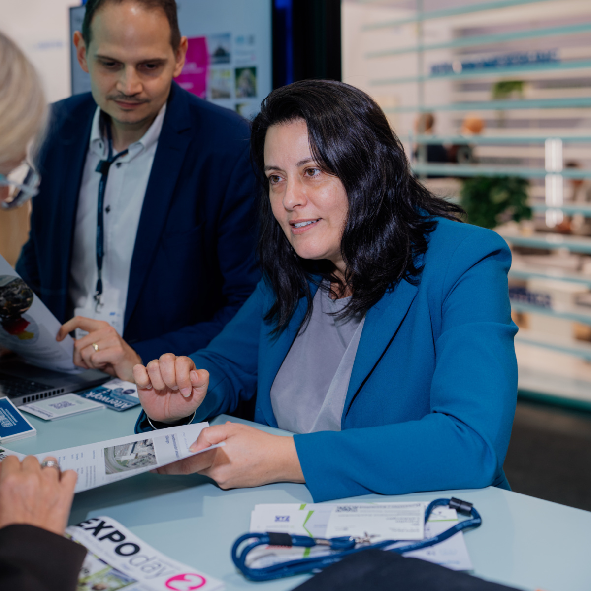 Eine Frau hält ein Blatt in der Hand und unterhält sich mit einer anderen Frau, die gegenüber von ihr am Stand steht.