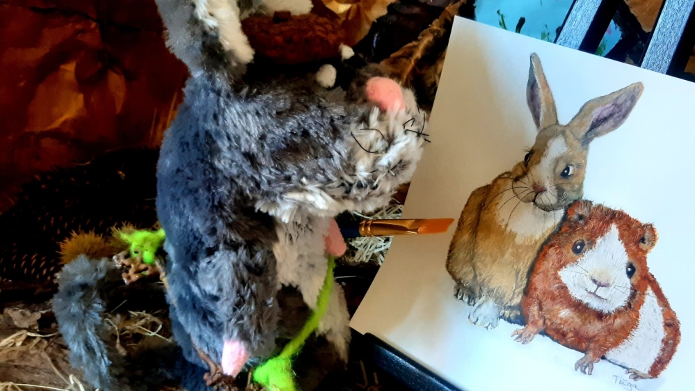 Emil Mausezahn malt Ein Stofftier mit einem Pinsel in der Hand, auf einer Leinwand ein Kaninchen und ein Meerschweinchen